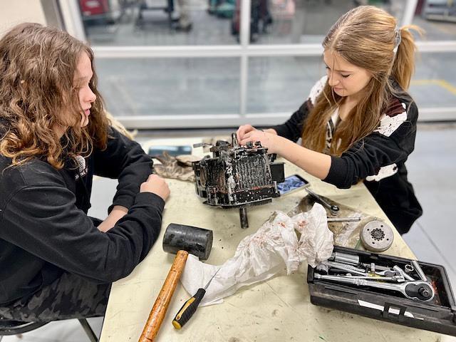 students working on small engine surrounded by tools